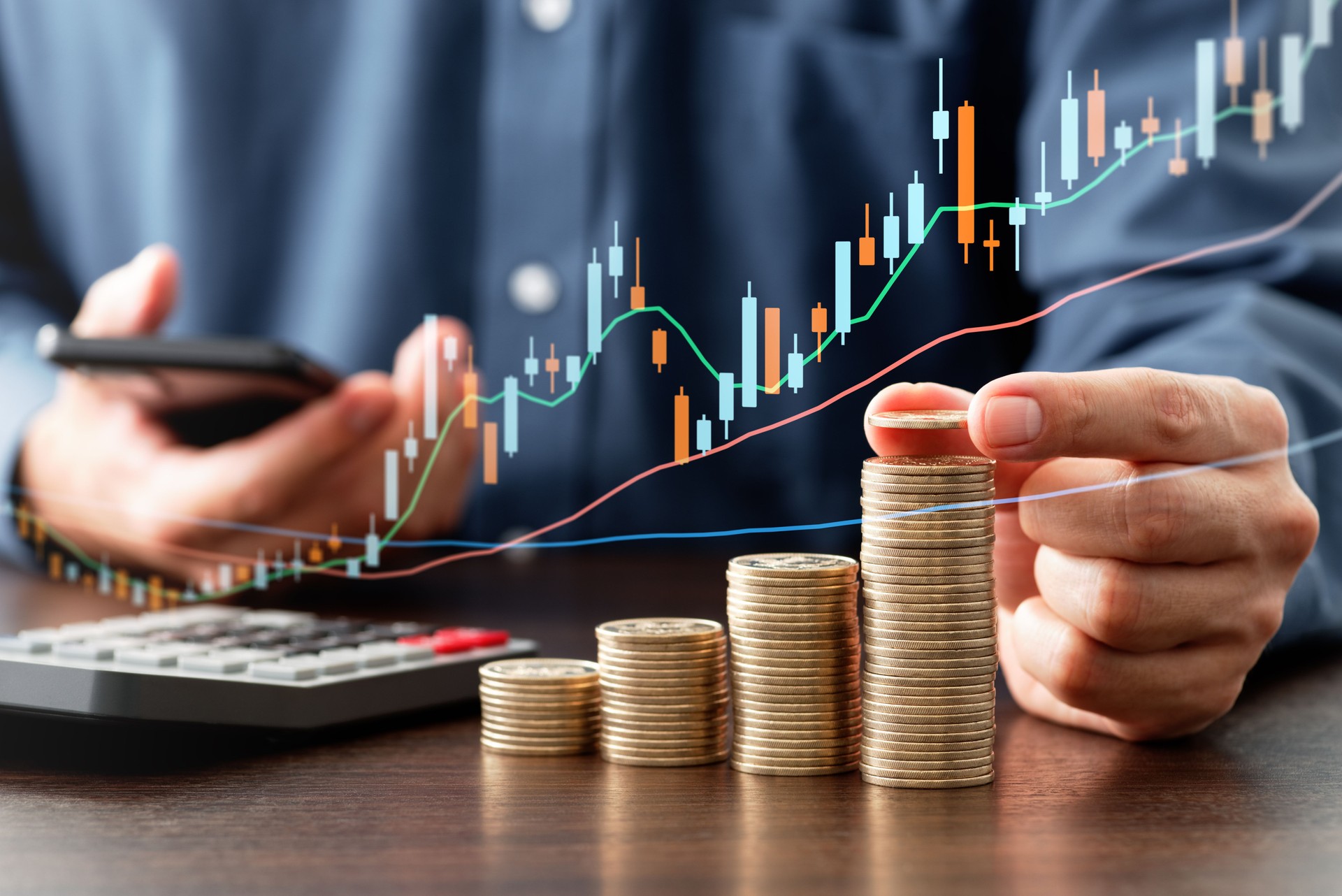 Stacked coins and candlestick chart. Person using smartphone and calculator.